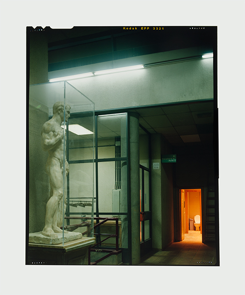 Una escultura de un hombre desnudo, encerrado en una urna de metacrilato parece mirar un servicio (WC) situado al fondo