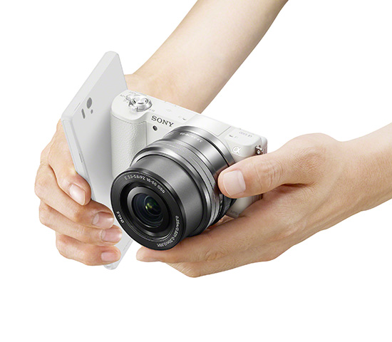 Unas manos sostienen una Sony A5100 blanca, mientras se conecta por NFC a un terminal móvil